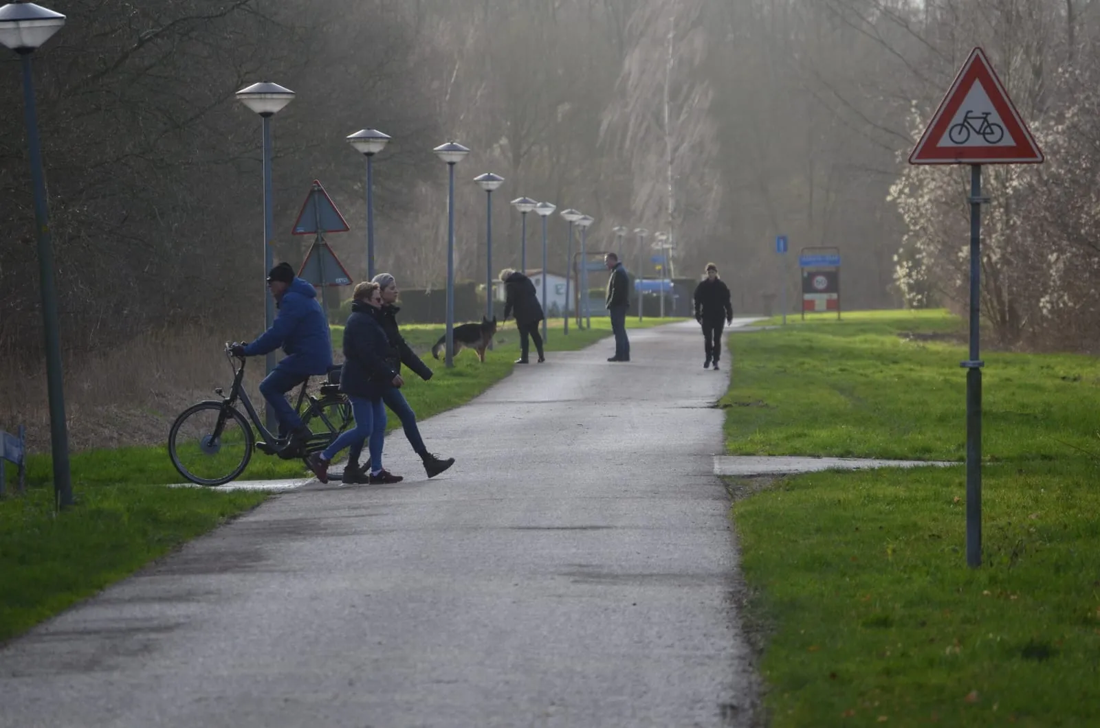 Op het fietspad langs het veld oefent een hond aan de lijn tussen fietsers en wandelaars